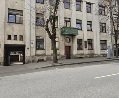 a building with a tree in front of a street at Kauno apartamentai king size bed in Kaunas