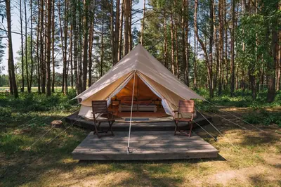 a tent with chairs on a wooden platform in a forest at Natur Camp Birštonas Small Cabins in Birštonas