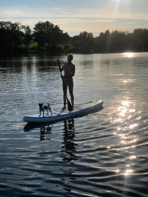 a man and a dog on a paddle board in the water at Pineplace trio BANGA in Žaugėdai