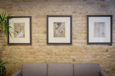 three framed pictures on a brick wall with a couch at New Town Home in Vilnius