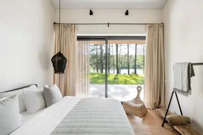 a bedroom with a bed and a large window at The Lake - Waterfront Villas Retreat in Mindūnai