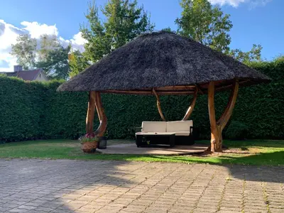 a large straw pavilion with a couch under it at Kepezinski ECO Apartments in Kaunas